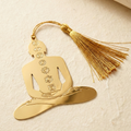 Gold Yogi bookmark with tassel on a textured beige background